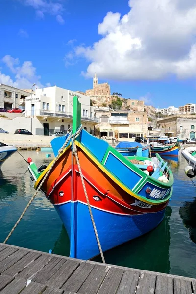 Традиционные рыболовные лодки в гавани с церковью Богоматери Лурдес на задней стороне, Мгарр, Гоцо, Мальта . — стоковое фото