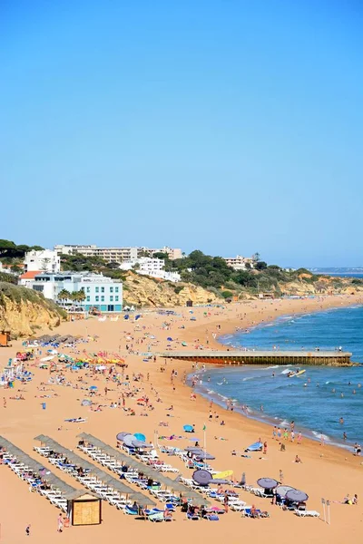Forhojd utsikt stranden med turister njuter de inställningen och stan byggnaderna till baksidan, Albufeira, Portugal. — Stockfoto