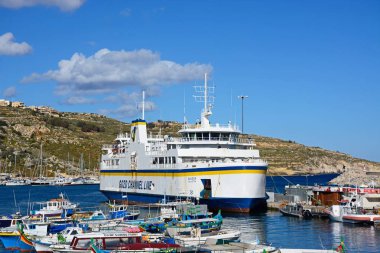 Arkayı Mgarr, Gozo, Malta limanında demirlemiş Gozo feribot ile renkli balıkçı teknesi limanda palamarla.