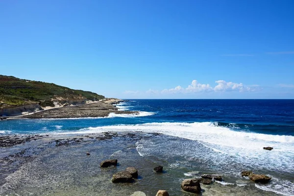 Zobrazit podél pobřeží s kameny v mělké vodě v popředí, Marsalforn, Gozo, Malta. — Stock fotografie