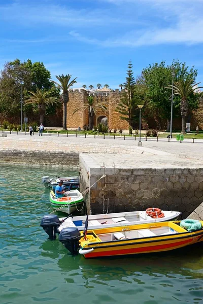 Vyn av entrén bågen av guvernörer slottet med små båtar förtöjda i förgrunden och turister njuter inställningen, Lagos, Portugal. — Stockfoto