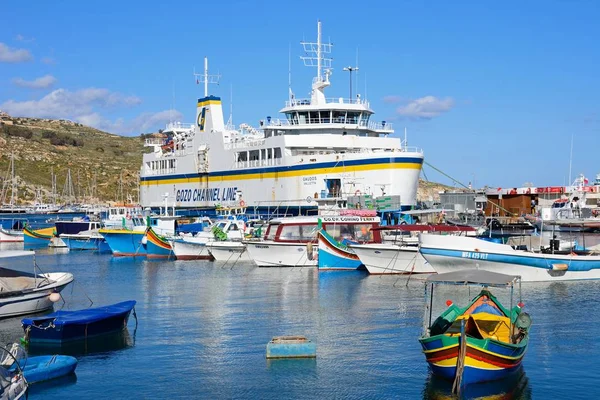 Bateau de pêche traditionnel maltais coloré Dghajsa amarré dans le port avec le ferry Gozo amarré dans le port à l'arrière, Mgarr, Gozo, Malte . — Photo