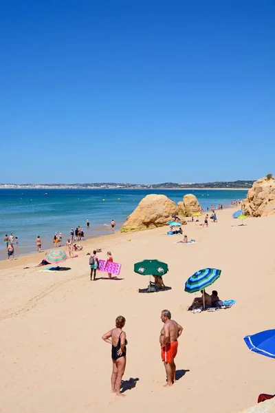 Relaxační turisté na pláži s velkými kameny a pohledy přes oceán směrem k pobřeží, Praia da Rocha, Portimao, Portugalsko. — Stock fotografie