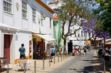 Turistler alışveriş caddesi jakaranda ağaçları tam Bloom, Lagos, Algarve, Portekiz ile eski bir şehir boyunca yürüyüş.