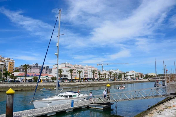 Paar lopen op een helling van een jacht afgemeerd aan de rivier Bensafrim met uitzicht op de promenade, Lagos, Algarve, Portugal. — Stockfoto