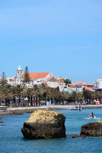 Вид вдоль реки Бенсафрим с променадом и прибрежными зданиями слева и скалами в море на переднем плане, Лагуш, Алгарве, Португалия . — стоковое фото