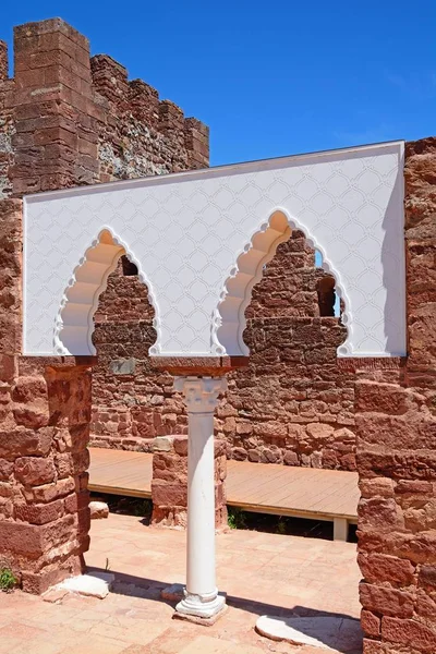 View of the Medieval ruins inside the castle showing the vaulted Moorish windows of the palace of balconies with the battlements and one of the towers to the rear, Silves, Portugal.