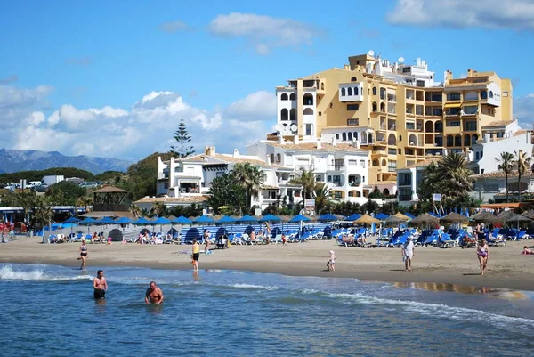 Turistas relajados en la playa con apartamentos en la parte trasera, Cabopino, Marbella, España . — Foto de Stock