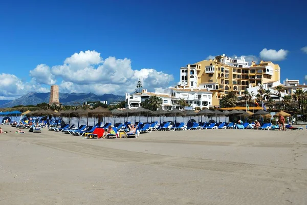 Turistas relajándose en la playa con apartamentos y una antigua torre de vigilancia en la parte trasera, Cabopino, Marbella, España . — Foto de Stock