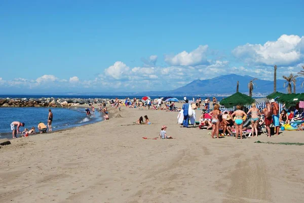 Turistas relajados en la playa con vistas hacia el mar y las montañas, Cabopino, Marbella, España . — Foto de Stock