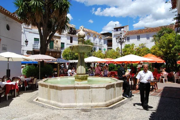 Stenen fontein met toeristen ontspannen op de stoep cafes in Orange Square, Marbella, Spanje. — Stockfoto