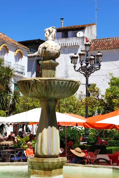 Stenen fontein met toeristen ontspannen op de stoep cafes in Orange Square, Marbella, Spanje. — Stockfoto