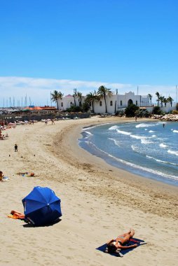 Daitona sahilinde dinlenen turistler, marinayla birlikte arkada, Marbella, İspanya.