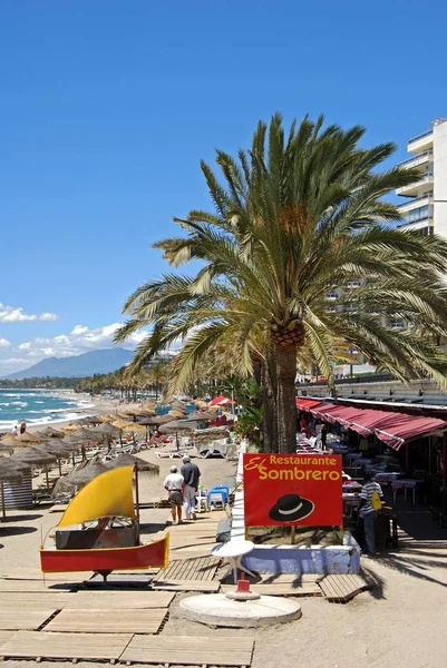 Turistas relajados en la playa de Daitona con restaurantes a la derecha, Marbella, España . — Foto de Stock