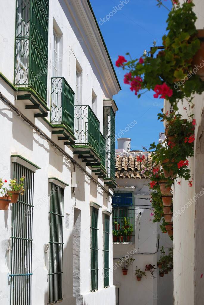 View down old town street with geraniums in pots on the walls, Arcos de la Frontera, Spain.