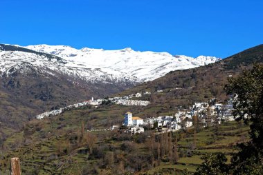 Sierra Nevada, Las Alpujarras, Granada Eyaleti, Endülüs, İspanya ve Avrupa 'nın kar örtülü dağlarının arka planında Capileira kasabası ile Bubion' un manzarası görülüyor..