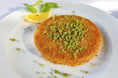 Geleneksel Türk kunefe tatlısını rendelenmiş şam fıstığı, dilimlenmiş limon ve nane ile kapatın..