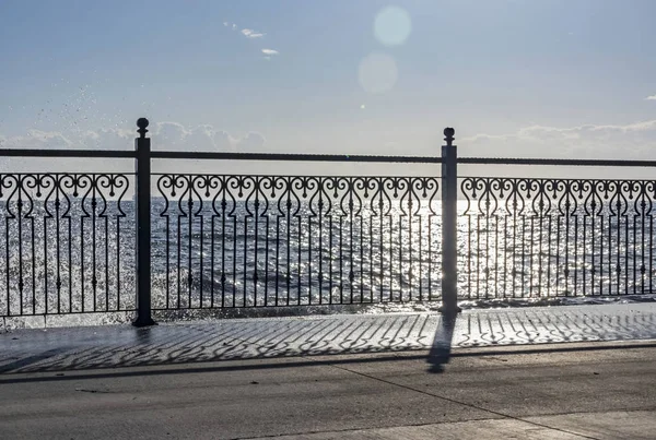 wrought iron railing at the pier and shadows with sunlight and waves