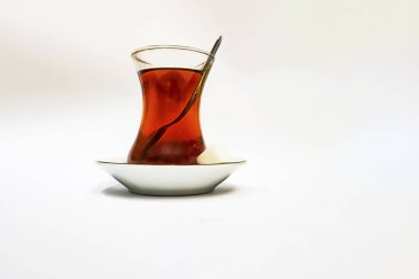 Cam fincanlı geleneksel Türk çayı, porselen tabak, şeker küpleri ve beyaz arka planda çay kaşığı.