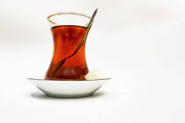 Cam fincanlı geleneksel Türk çayı, porselen tabak, şeker küpleri ve beyaz arka planda çay kaşığı.