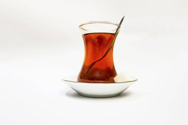 Cam fincanlı geleneksel Türk çayı, porselen tabak, şeker küpleri ve beyaz arka planda çay kaşığı.