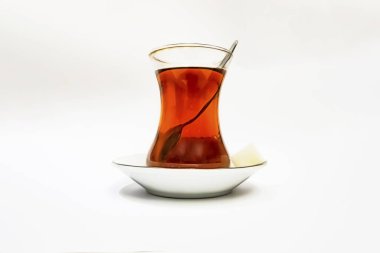 Cam fincanlı geleneksel Türk çayı, porselen tabak, şeker küpleri ve beyaz arka planda çay kaşığı.