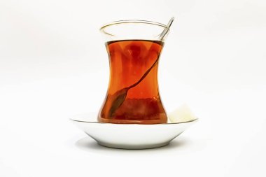 Cam fincanlı geleneksel Türk çayı, porselen tabak, şeker küpleri ve beyaz arka planda çay kaşığı.