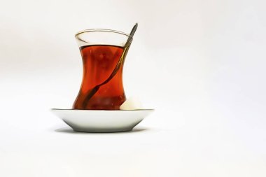 Cam fincanlı geleneksel Türk çayı, porselen tabak, şeker küpleri ve beyaz arka planda çay kaşığı.