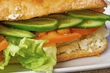 Marullu, peynirli, dilimlenmiş domatesli ve beyaz tabakta salatalıklı sandviç yemeye hazır..