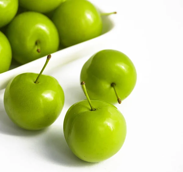 Green sour plums in the plate, plum pictures on the white ground,