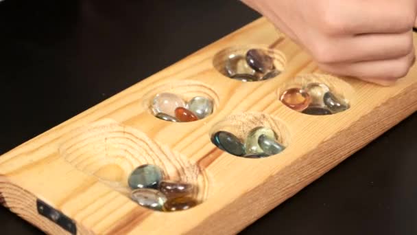木製のマンガラゲーム マンガラゲームボードとガラスのビー玉 黒の背景に — ストック動画