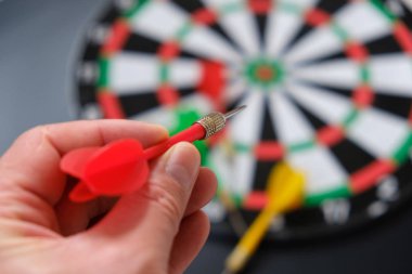 Yeşil dart, dart tahtası ve okla nişan alan bir adamın ellerinde okuyun.,