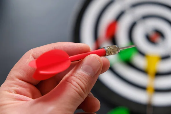 Read in the hands of a man taking aim with green darts, dart board and darts,