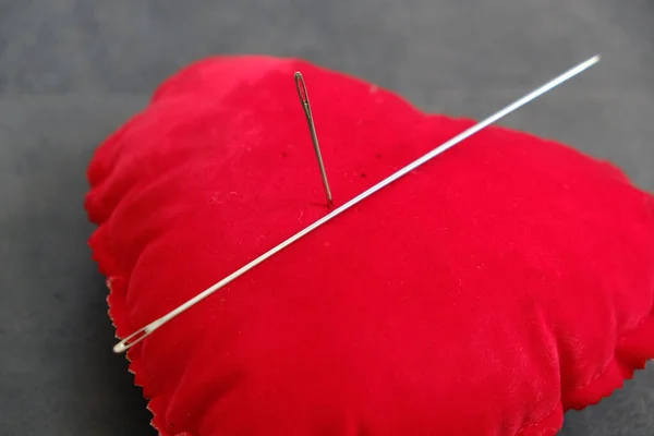 red pincushion and a large sewing needle, needle spell,