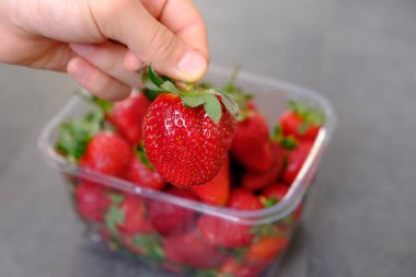 Gri ahşap arka planda, plastik kutuda 1 kilo taze çilek.