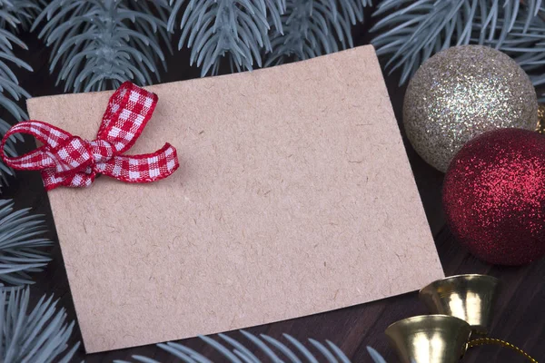 Navidad Navidad Año Nuevo Concepto de tarjeta de felicitación de vacaciones con hoja vacía de cartón Navidad bolas rojas y doradas arco de campana lazos de abeto ramas sobre fondo de madera oscura, espacio para el texto — Foto de Stock