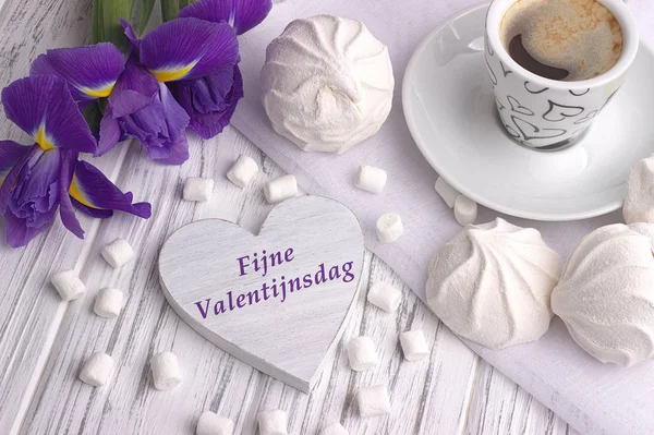 Νεκρή φύση με φλιτζάνι καφέ marshmallow zephyr ίριδας λουλούδια καρδιά πινακίδα με γράμματα ευτυχισμένη ημέρα του Αγίου Βαλεντίνου στα Ολλανδικά σε άσπρο φόντο ξύλινη. — Φωτογραφία Αρχείου