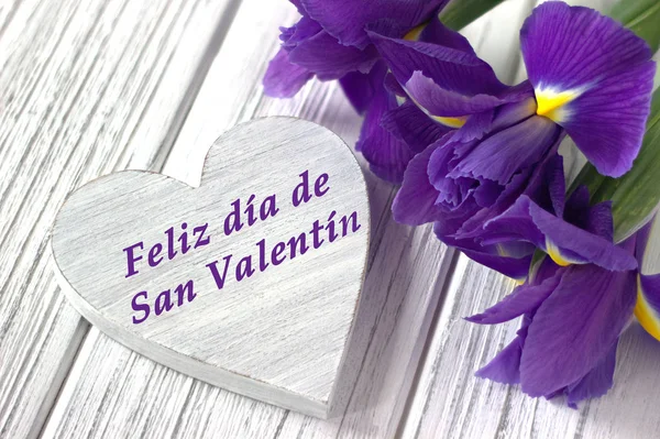 Bodegón con signo de corazón flores de iris sobre fondo de madera blanca. Boda. Tarjeta de felicitación del día de San Valentín con texto Feliz día de San Valentín en español —  Fotos de Stock