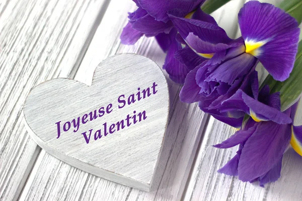 Νεκρή φύση με καρδιά τα λουλούδια της ίριδας σύμβολο σε άσπρο φόντο ξύλινη. Γάμου. Ημέρα του Αγίου Βαλεντίνου ευχετήρια κάρτα με κείμενο ευτυχισμένη ημέρα του Αγίου Βαλεντίνου στα Γαλλικά. — Φωτογραφία Αρχείου