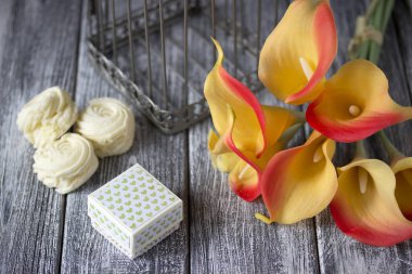 gri bir ahşap zemin üzerine hatmi ve karton kutuyla turuncu sarı calla zambak buketi.