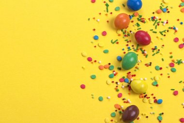 Çikolata Paskalya yortusu yumurta ile şeker ve tatlılar sarı renkli arka plan üzerinde renkli patlama.