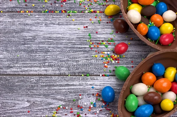 Easter chocolate egg with colorful explosion of candies and sweets on gray colored wooden background.