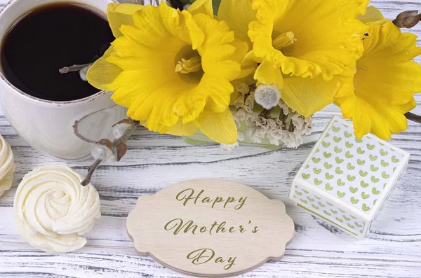Xícara de café com marshmallow, caixa de presente verde, flores amarelas no fundo de madeira branco e lettering feliz dia da mãe . — Fotografia de Stock