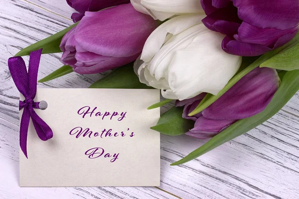 Tulipas roxas e brancas com papel branco em um fundo de madeira branco e lettering cartão feliz Dia das Mães . — Fotografia de Stock