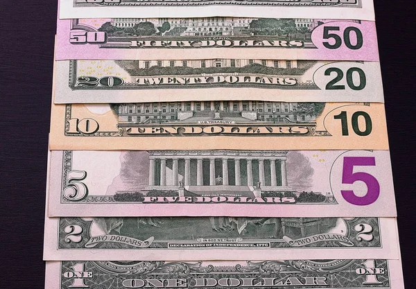 Stapel von Dollarscheinen verschiedener Stückelungen auf schwarzem Hintergrund. — Stockfoto