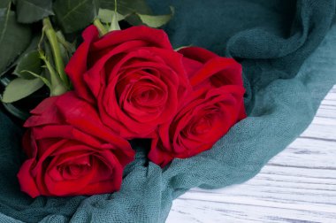 Beyaz ahşap zemin üzerine yeşil Tekstil üzerinde üç kırmızı gül.