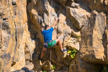 Male rock climber climbing up a cliff clipart