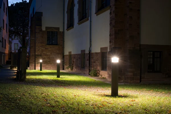 Outdoor bollard lights in front of an old administration building illuminating a walkway in the garden at night — Stock Photo, Image