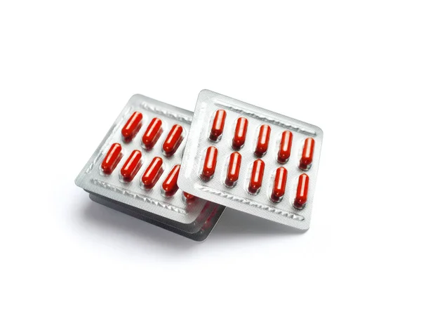 Капсулы с красными таблетками в пузырьках на белом фоне — стоковое фото