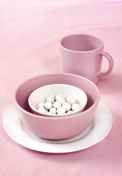 Vaisselle rose et blanche avec des dragees de sucre à l'intérieur sur un chiffon rose — Photo